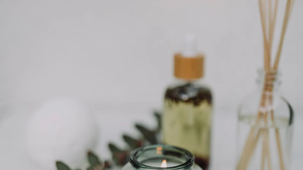 Small glass bottle of essential oil with a reed diffuser setup on a pale surface