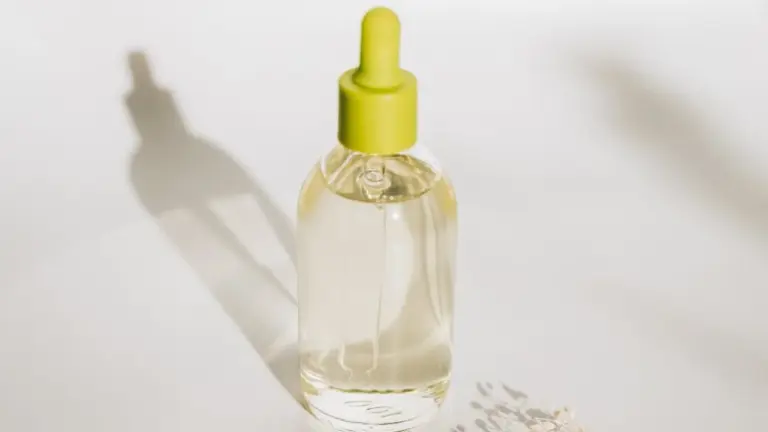 Dropper bottle of cuticle oil with a yellow cap on a white surface.