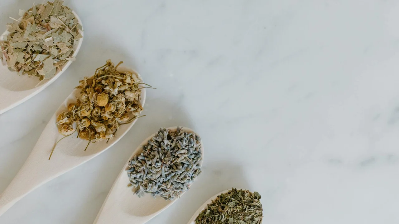 Dried herbs arranged in white spoons on a light marble surface, ready for diffuser blends.