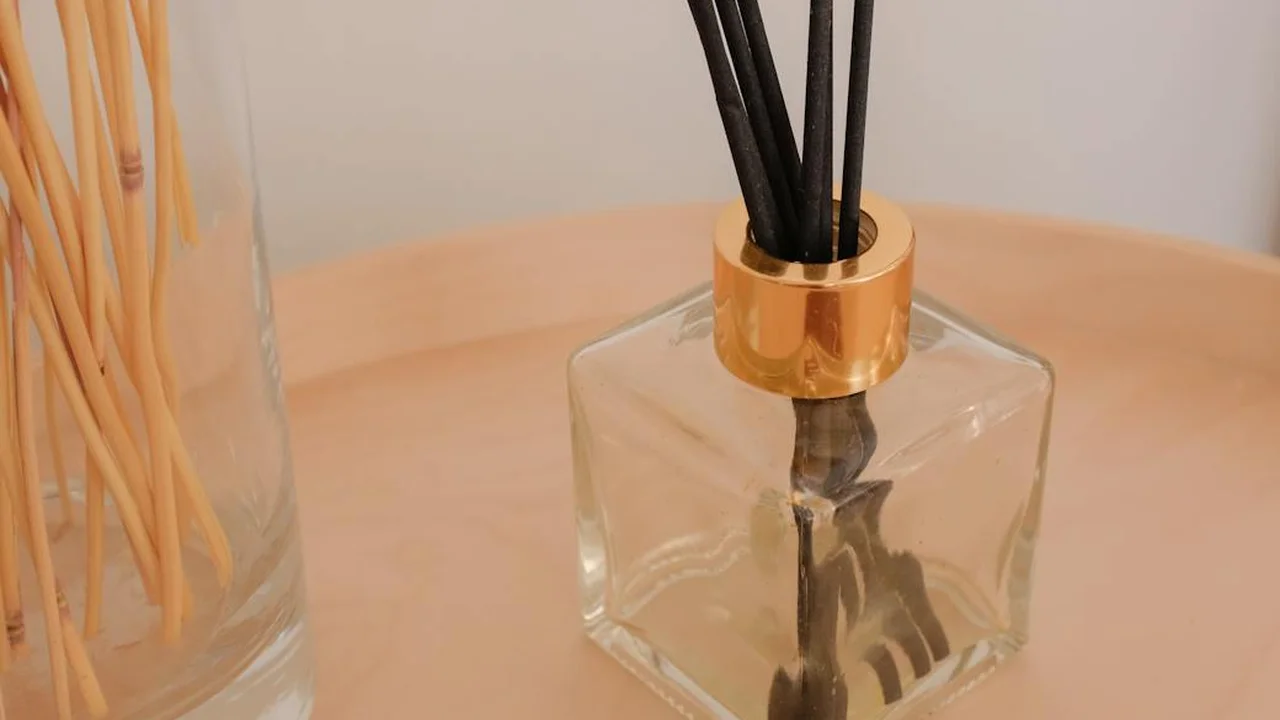Close-up of a glass reed diffuser with black reeds and a wooden cap on a light wooden surface