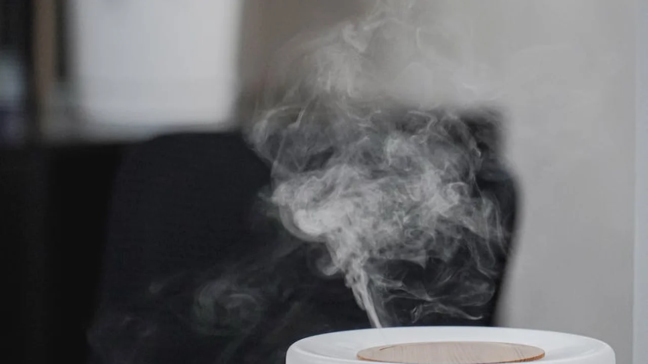A white essential oil diffuser releasing a plume of mist in a modern indoor setting
