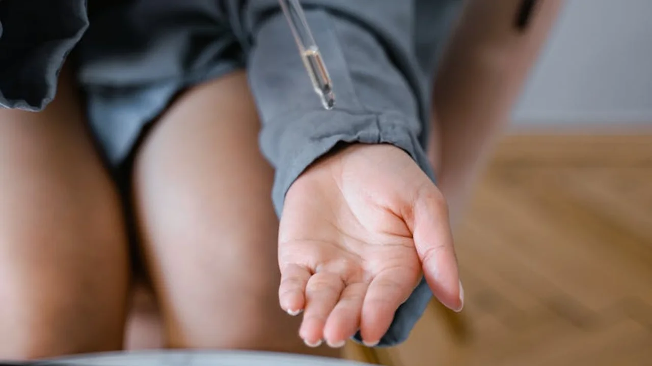 Close-up of a hand holding a dropper above another hand, suggesting skincare application or natural remedies.