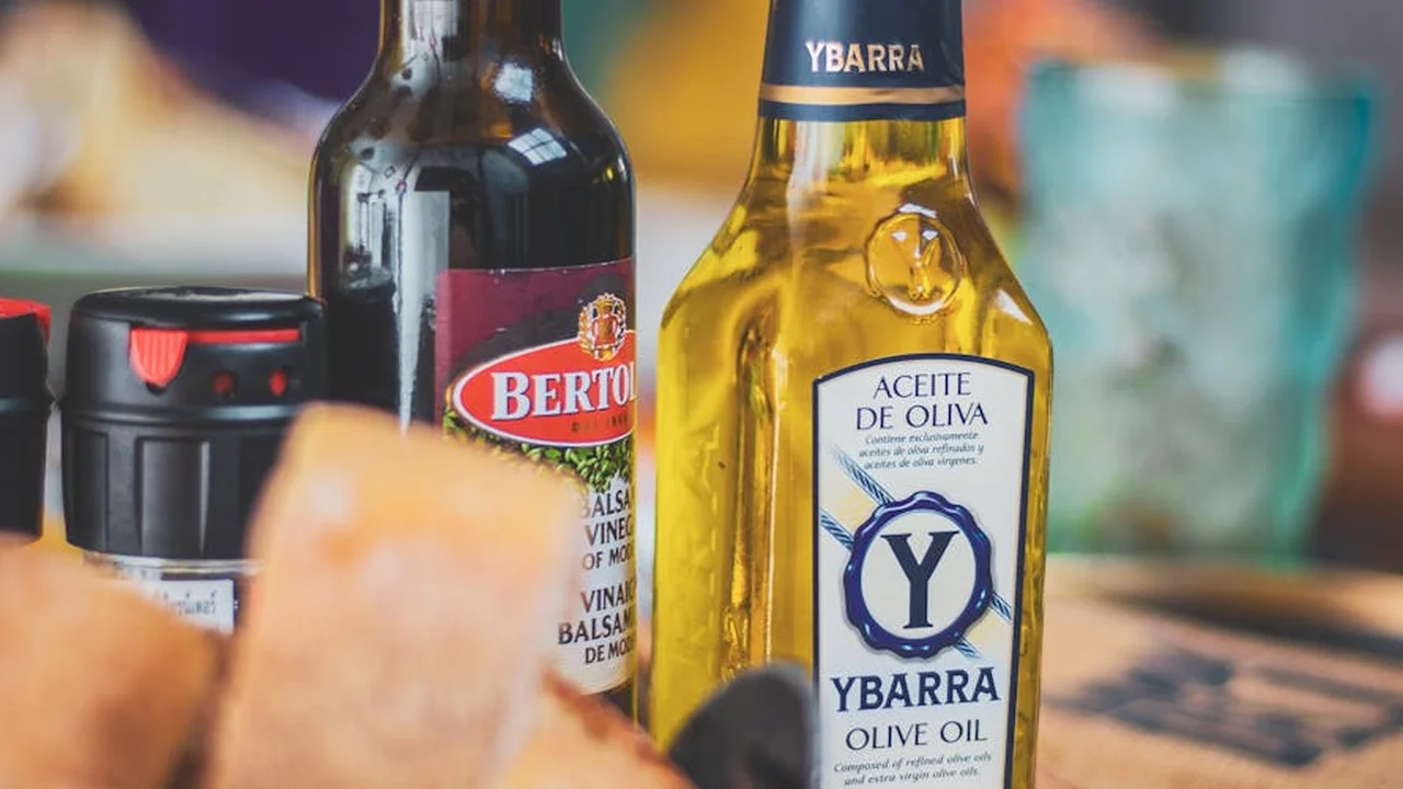 Close-up of several cooking oil bottles on a kitchen table, including a Bertolli dark bottle and a Ybarra olive oil bottle.