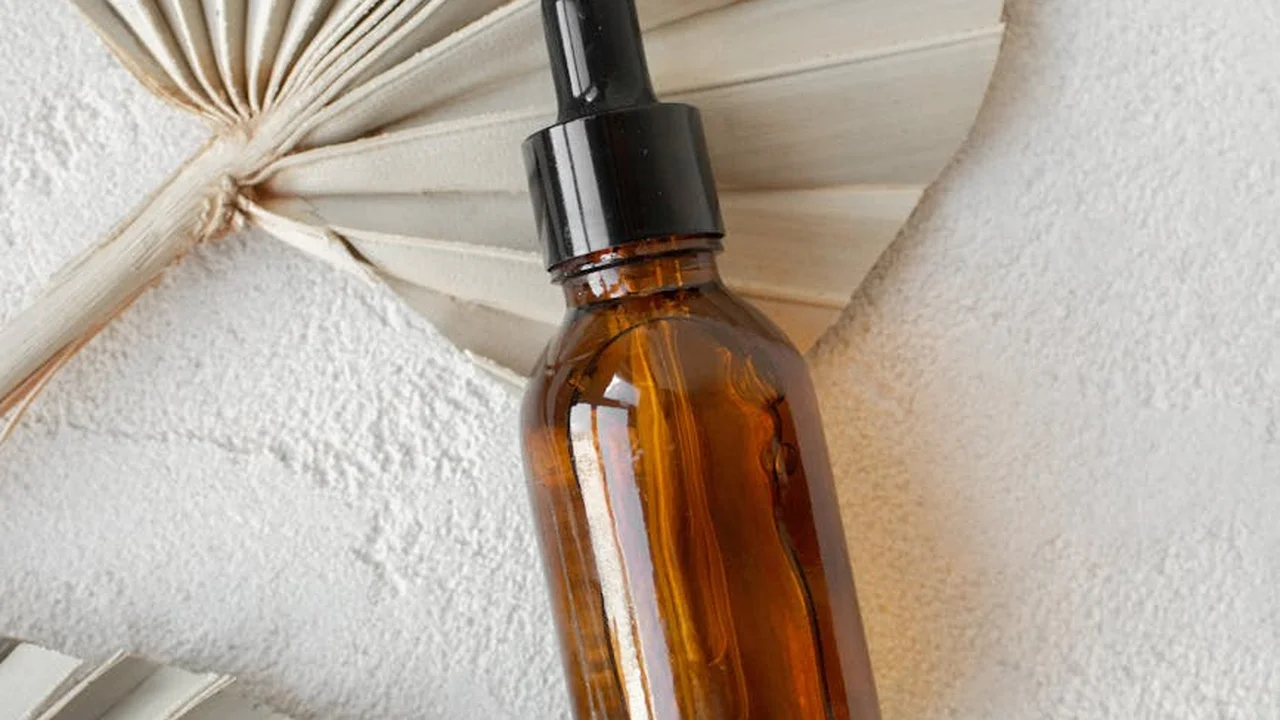 Amber glass dropper bottle of essential oil on a textured white surface with a dried palm leaf in the background.