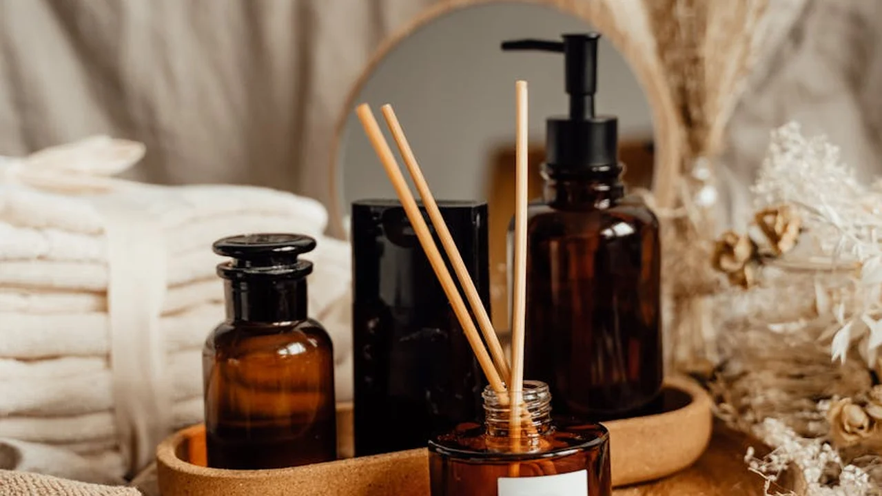Amber glass essential oil bottles and a reed diffuser on a wooden tray in a cozy home setting, suggesting non-plug-in aroma options
