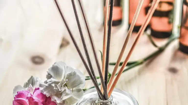 Reed diffuser with essential oil bottles in the blurred background on a light wooden surface.