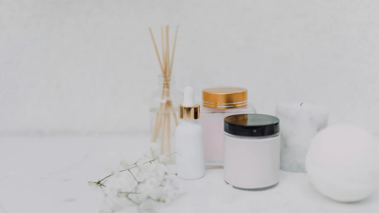 A minimalist white setup with essential oil diffuser components, including a reed diffuser, small white bottles, and jars arranged on a clean surface.