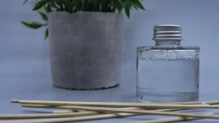 Reed diffuser sticks and a glass bottle of essential oil in the foreground with a potted plant in the background.