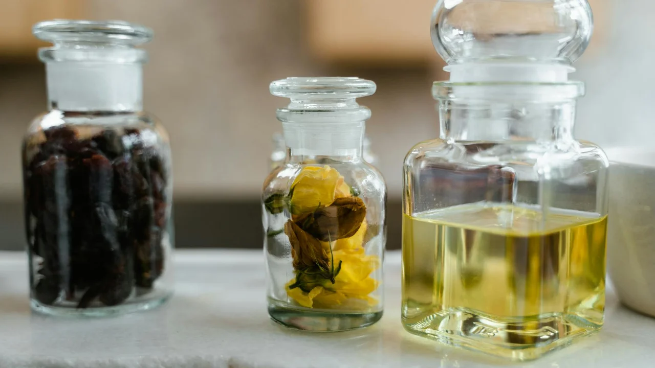 Three glass apothecary bottles with dark liquid, botanicals, and pale oil on a neutral surface.