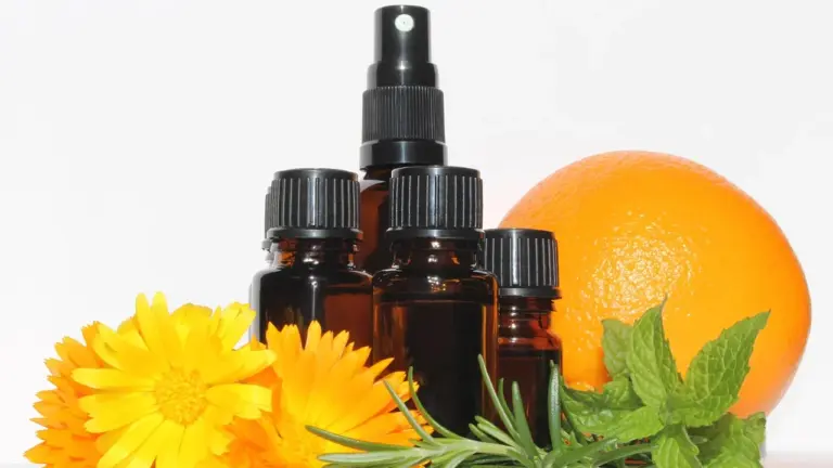 Brown glass essential oil bottles with a spray top, an orange, and yellow flowers on a white background.