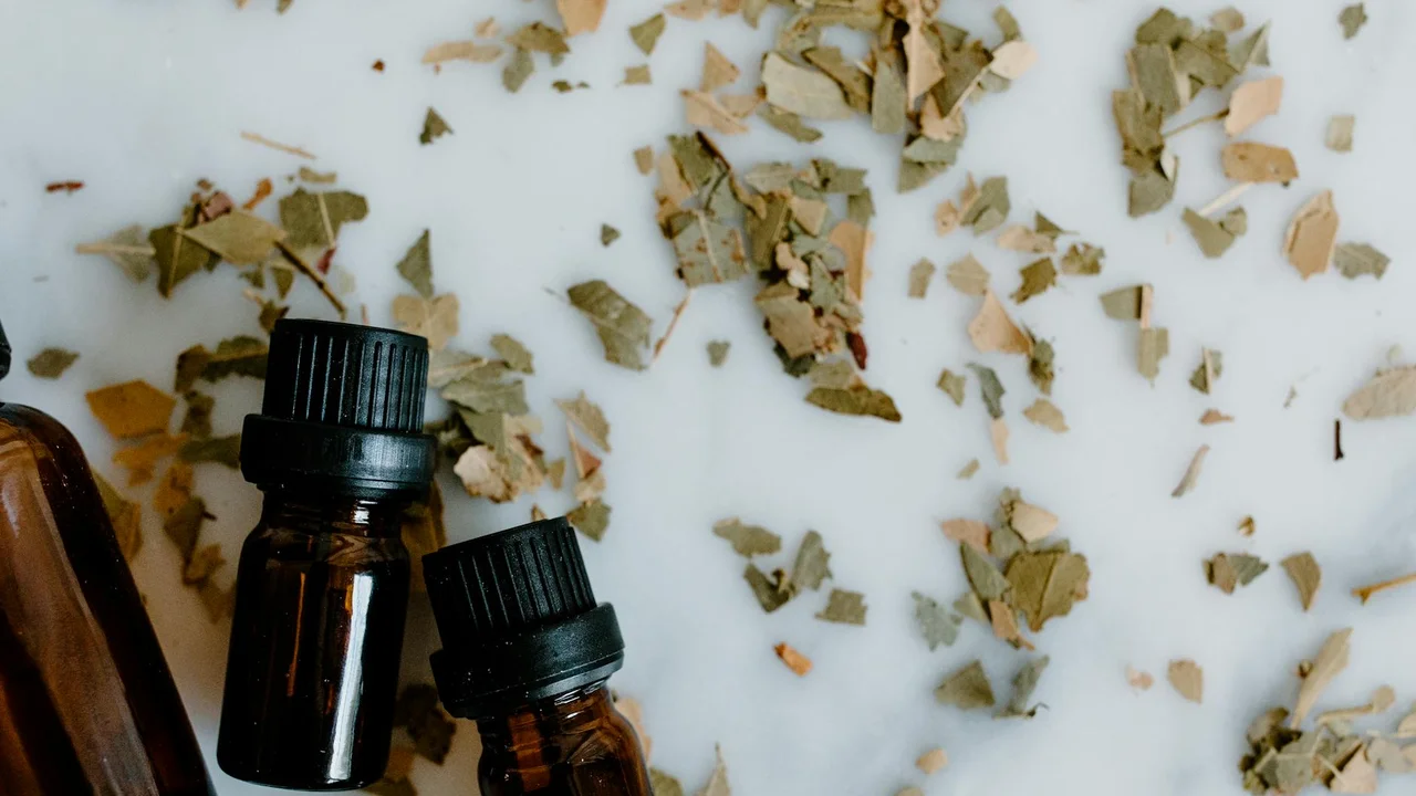 Two amber essential oil bottles with dried leaves scattered on a light surface