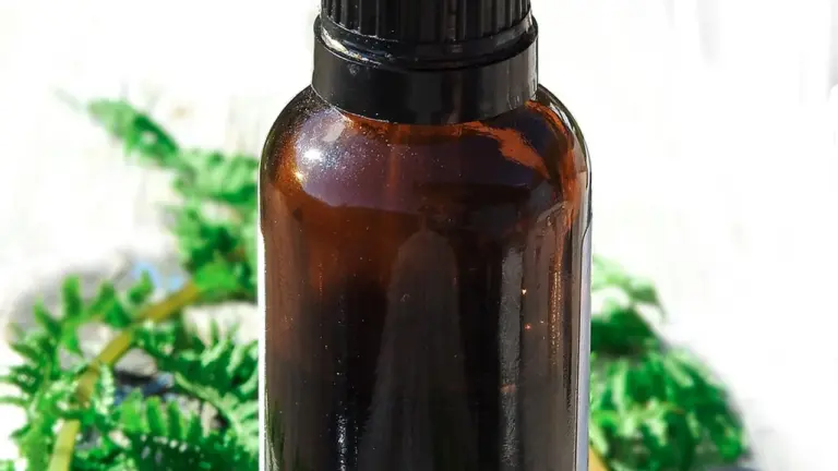 Close-up of a brown glass essential oil bottle with a black cap, on a light surface with blurred green foliage in the background.
