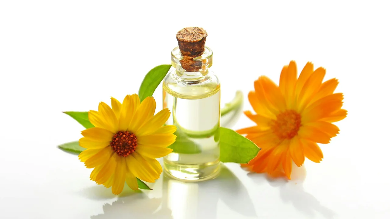 A small glass bottle of essential oil with a cork stopper, flanked by yellow-orange flowers on a white background.