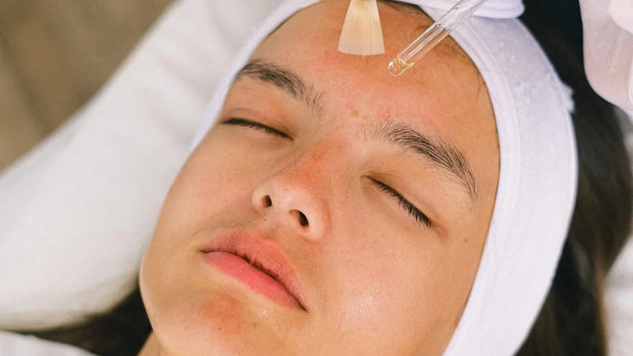 Close-up of a calm person with eyes closed during a spa facial as a dropper hovers over the forehead to apply oil.