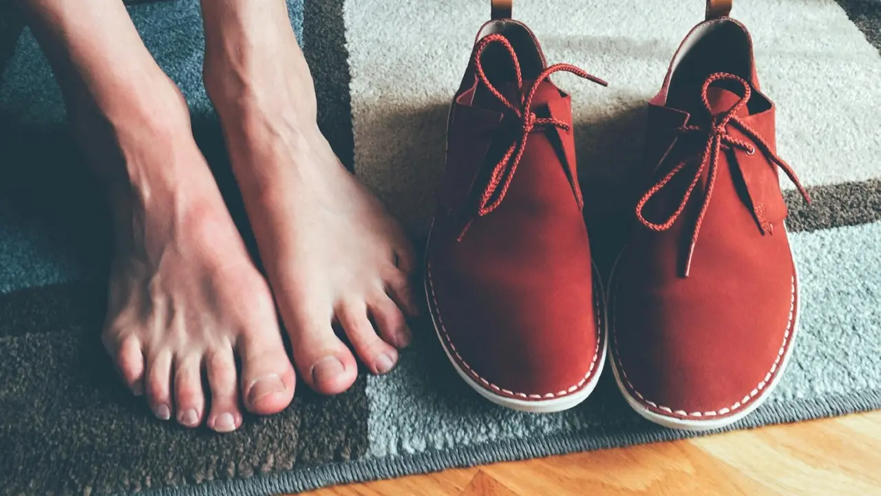 Bare feet beside a pair of red shoes on a textured rug, illustrating foot care context.