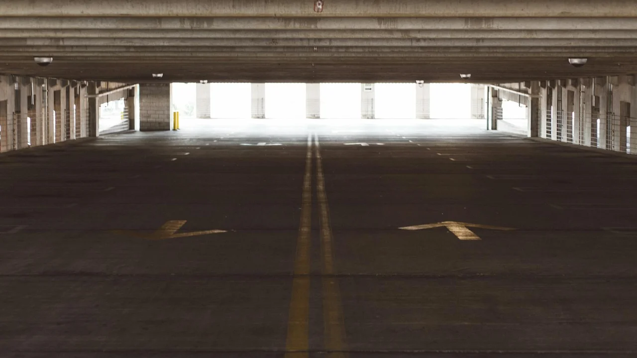 Dim concrete garage floor with faint oil stains and yellow center lines, representing a driveway or parking structure surface needing prompt cleanup.