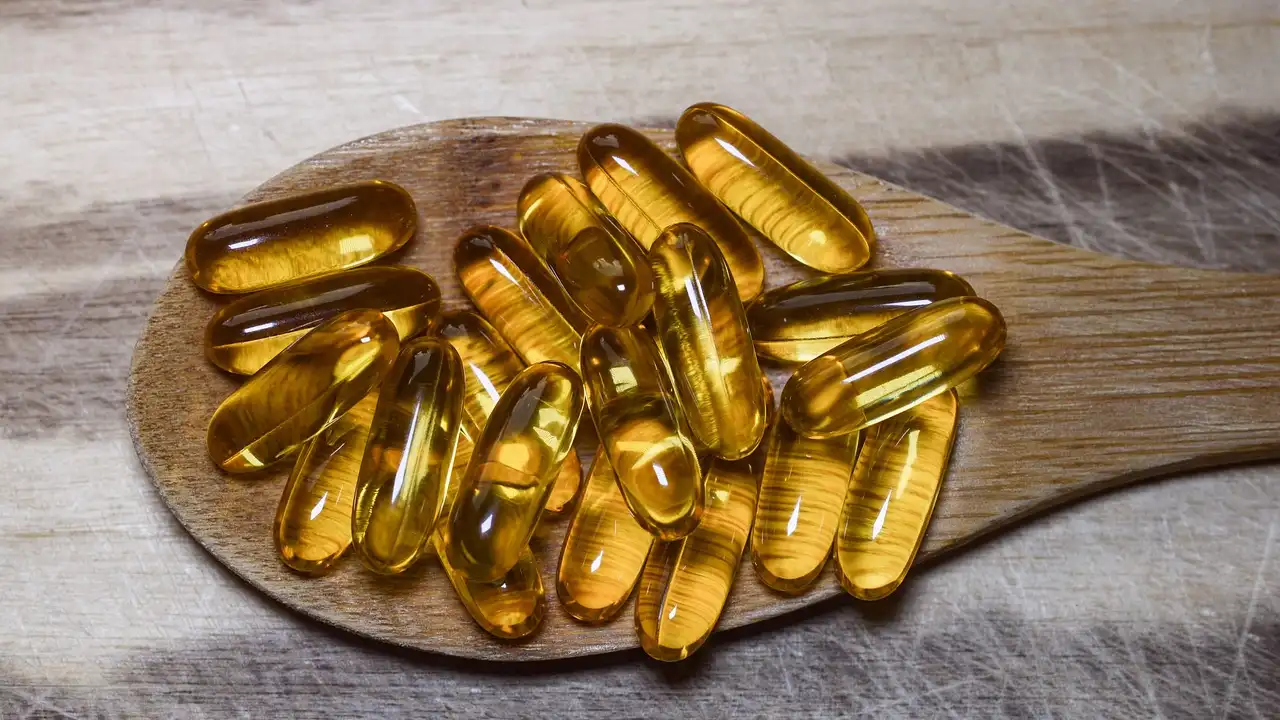 Golden fish oil capsules on a wooden spoon, representing dietary supplements