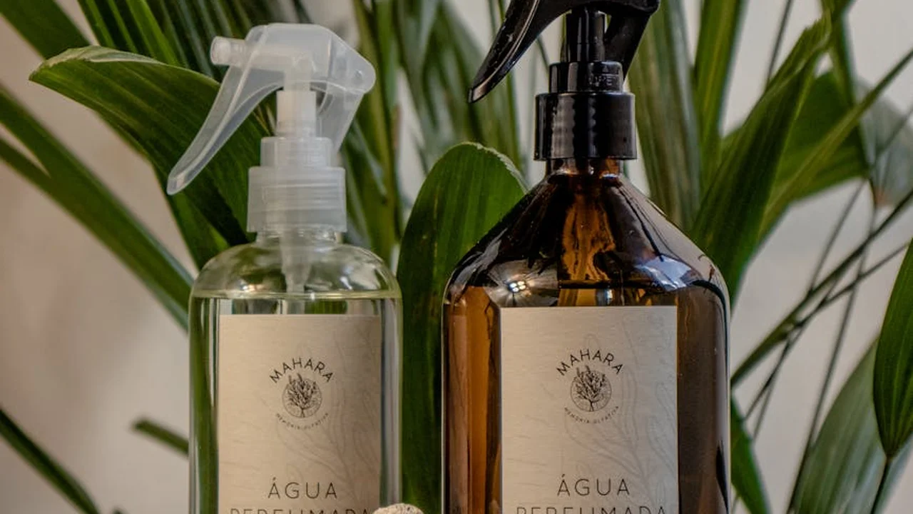 Two spray bottles (one clear, one amber) with fragrance labels, set among green leafy plants.