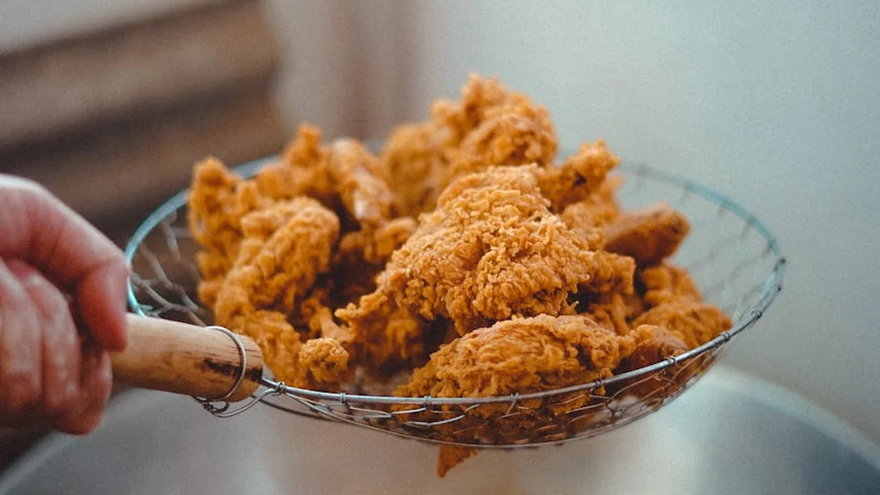 Crispy fried chicken pieces resting in a metal wire frying basket held by a hand.