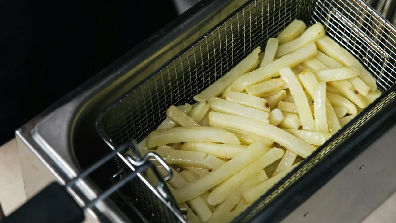 French fries placed in a metal fryer basket inside hot cooking oil.