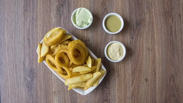 Plate of onion rings and French fries with three dipping sauces on a wooden table