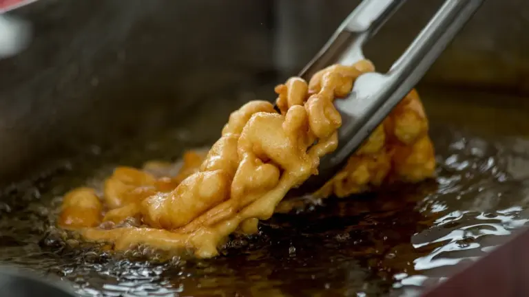 Battered food being fried in hot oil, held with tongs.