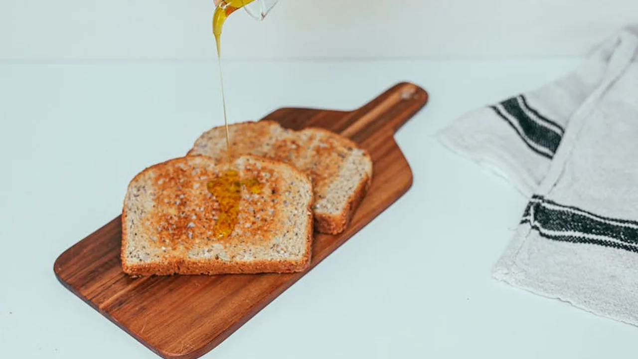 Two slices of bread on a wooden cutting board with oil being drizzled over them