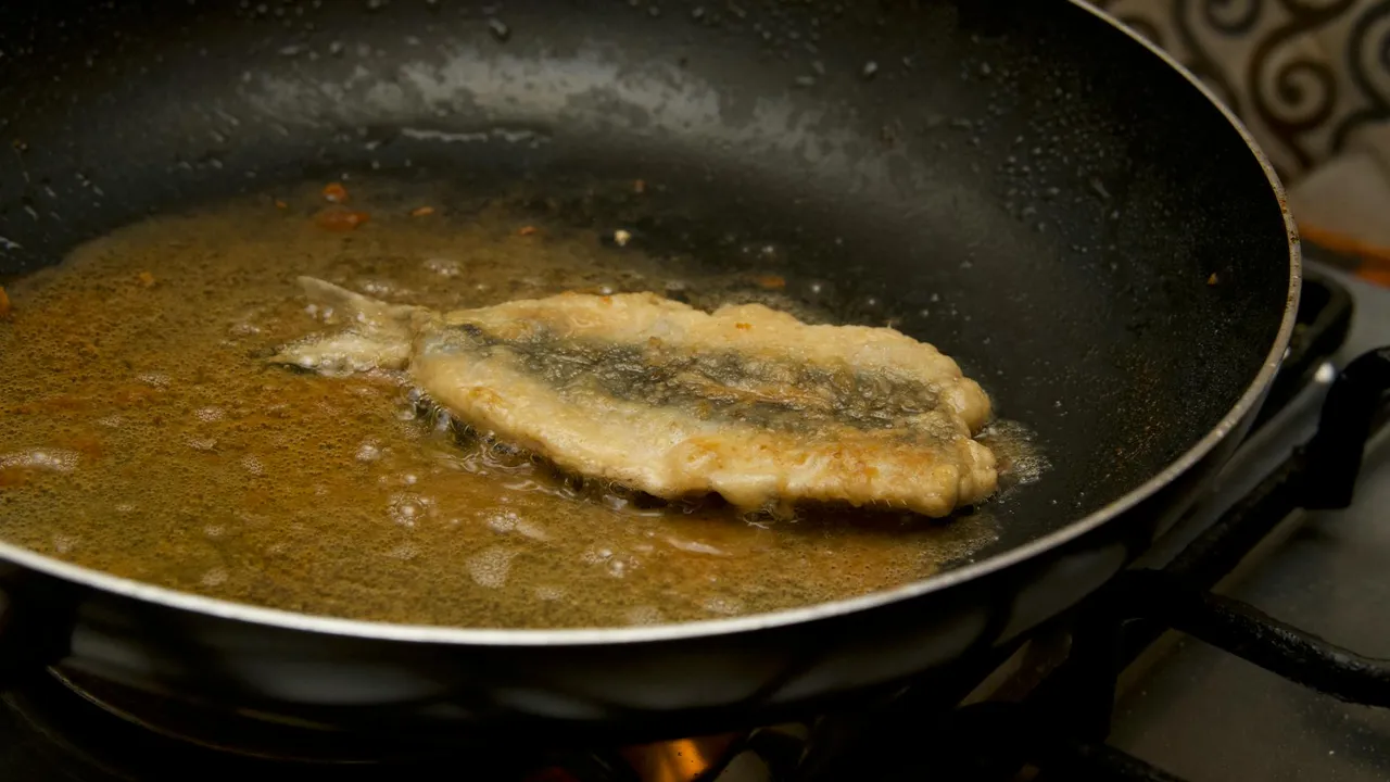 Fish fillet frying in oil in a skillet, with bubbling oil around it, illustrating oil's role in flavor development during cooking.