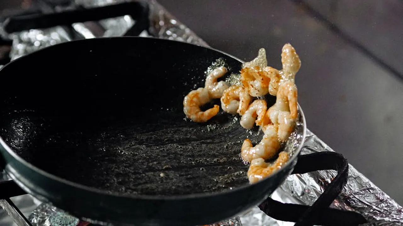 Cast-iron skillet with a few curled fried shrimp resting on foil-lined surface.