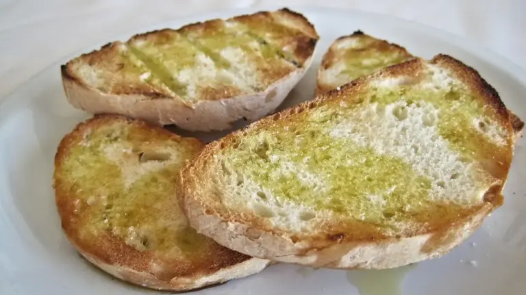 Three slices of garlic bread brushed with olive oil on a white plate.