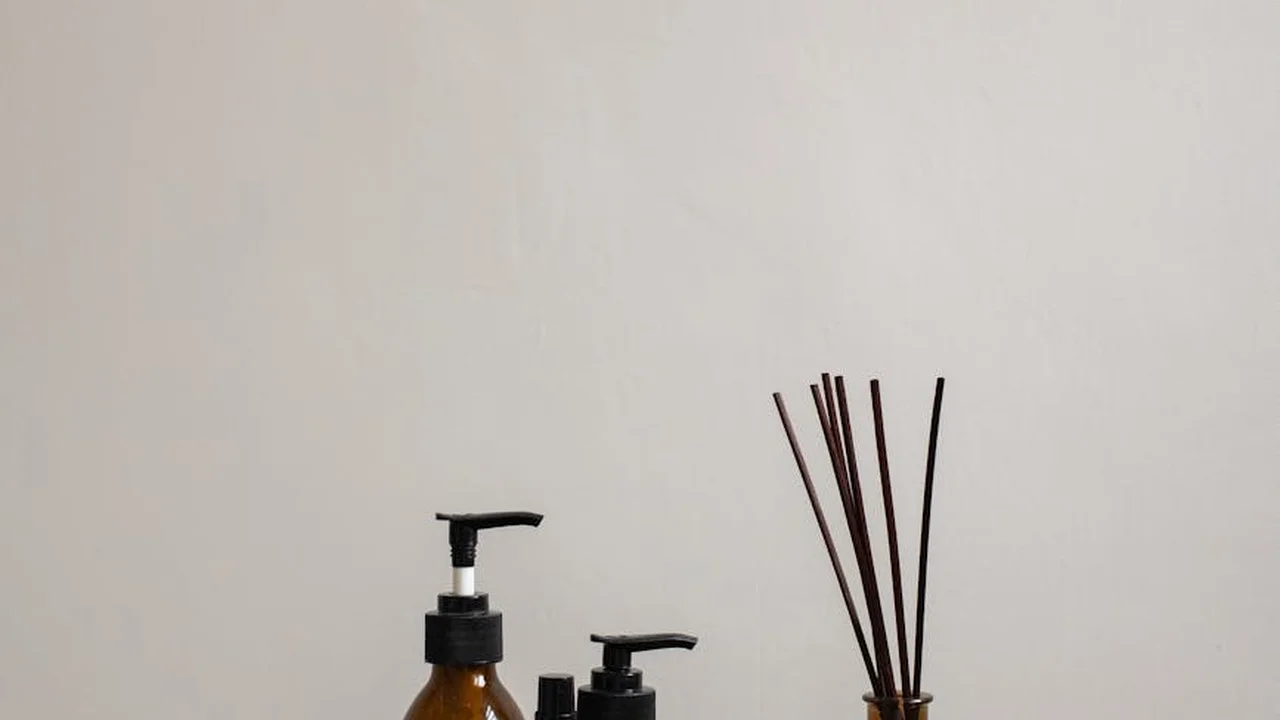 Minimalist image showing dark amber essential oil bottles and a diffuser set against a light background, suggesting non-comedogenic oils for acne-prone skin.