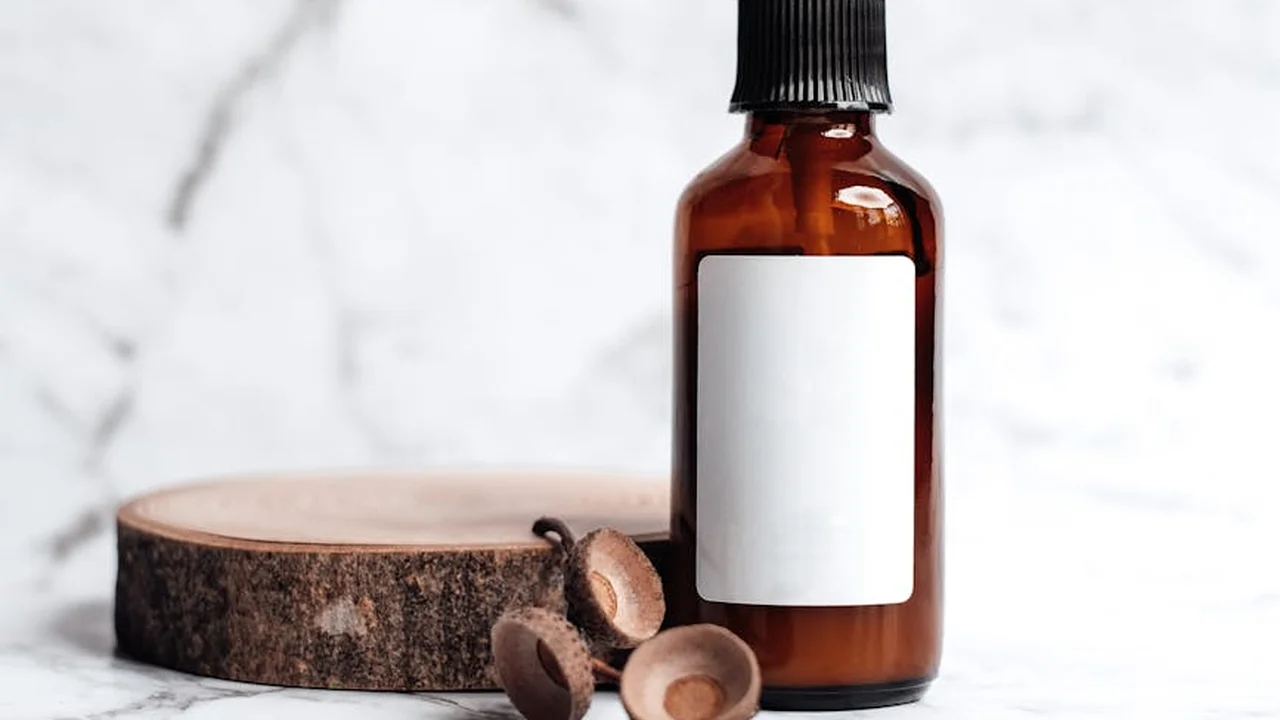 Amber glass essential oil bottle with dropper cap on a wooden coaster, set against a marble background.