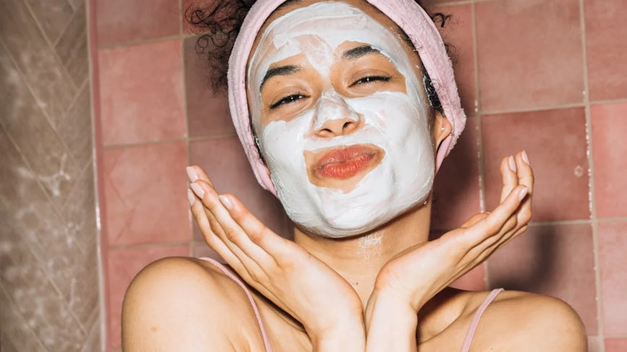Person wearing a white facial mask and a pink headband, posed in a pink-tiled bathroom.