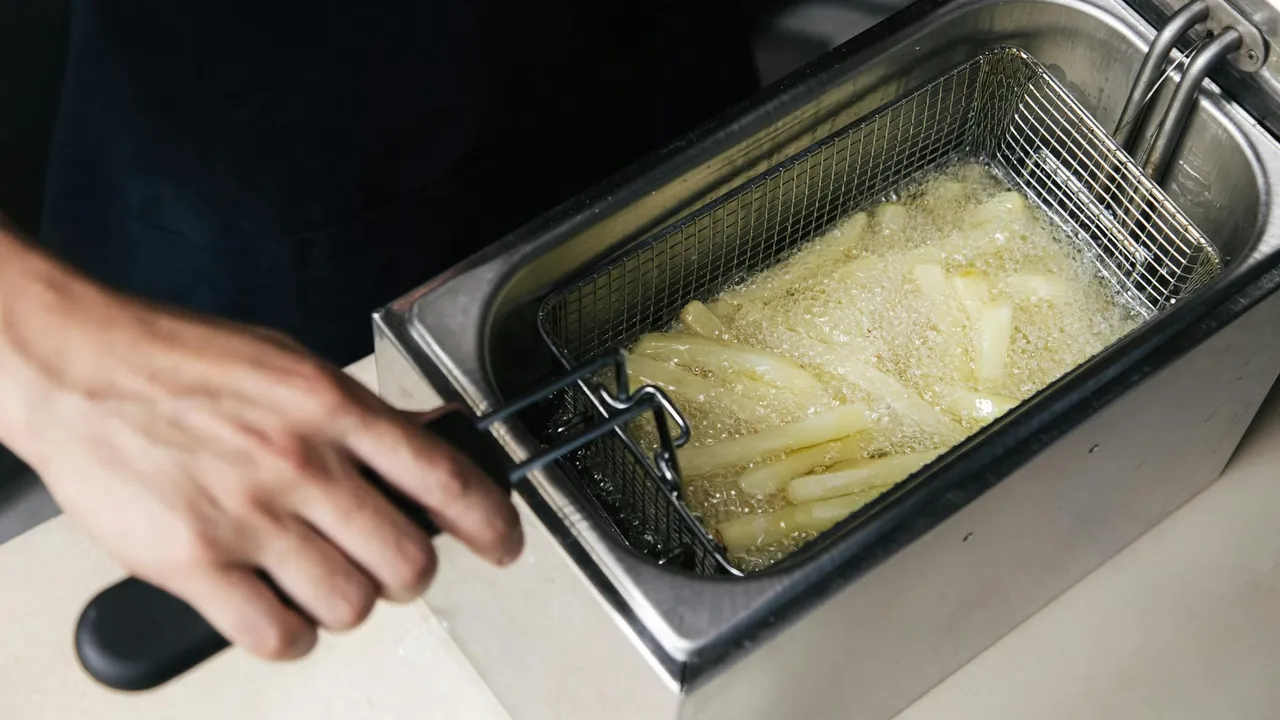 A person uses a metal fry basket to submerge food in a deep fryer with hot oil