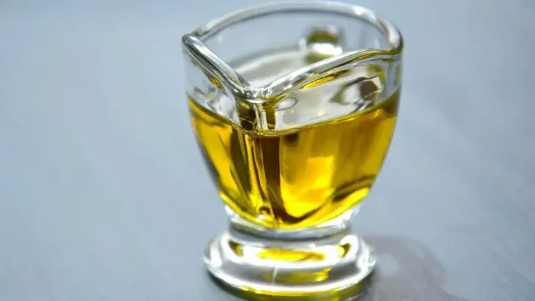 A small glass bottle filled with golden oil sits on a light gray surface.