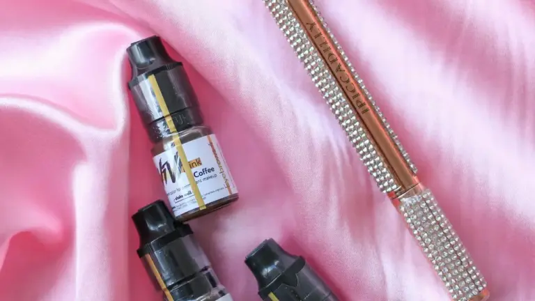 Close-up of two small glass dropper bottles on pink satin fabric; one bottle's label appears to read 'Coffee'.