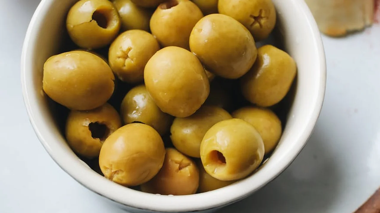 Bowl of green olives in a white dish on a light surface