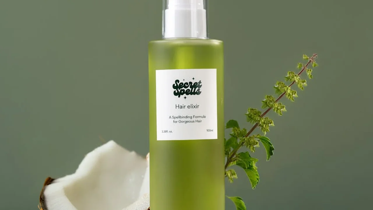 Green opaque bottle with a spray cap labeled 'hair elixir' on a muted green background, with a sprig of plant nearby.