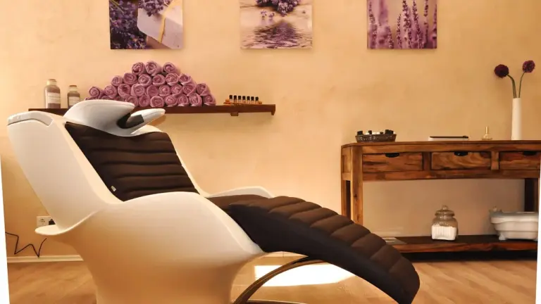 A clean, modern spa salon with a white reclining chair, wooden shelves, and purple flower decor.