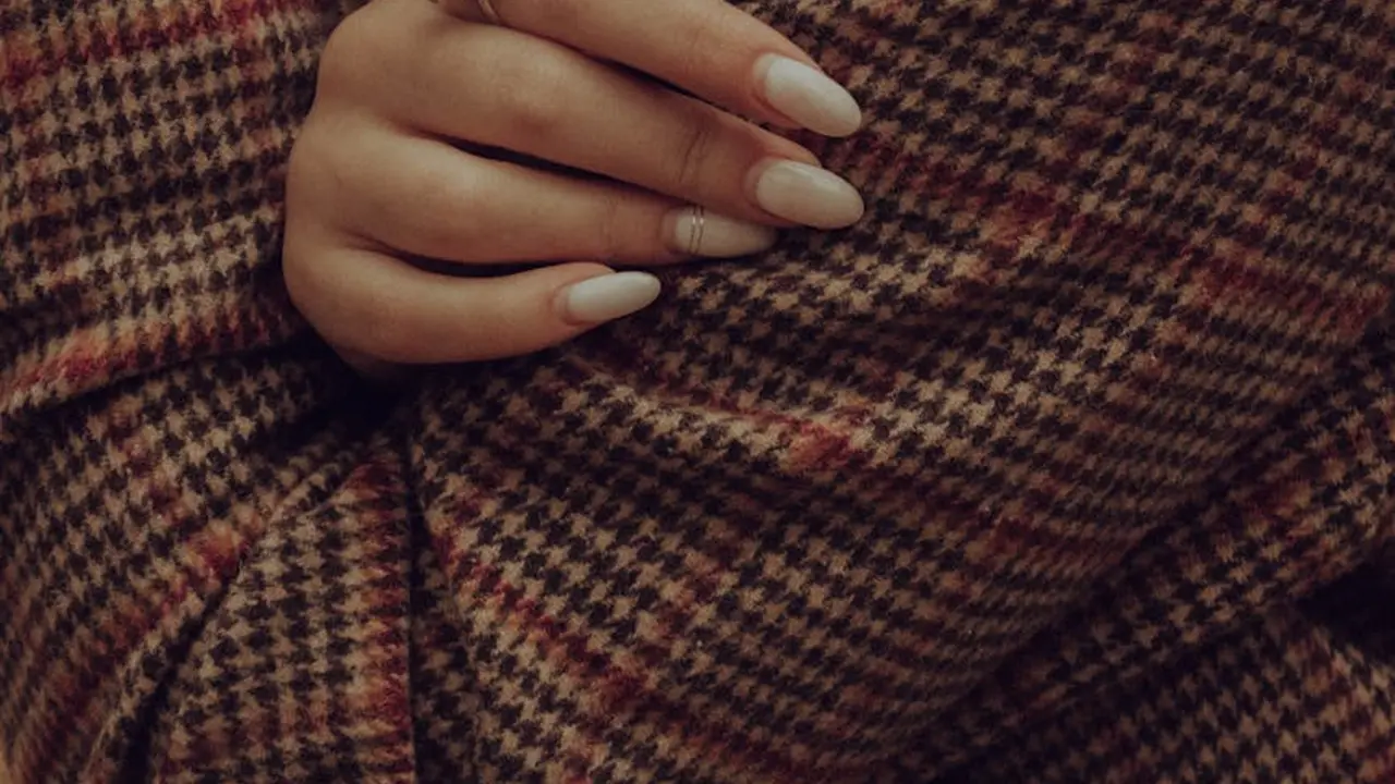 Close-up of a woman's hand with neatly manicured nails resting on a warm plaid fabric.