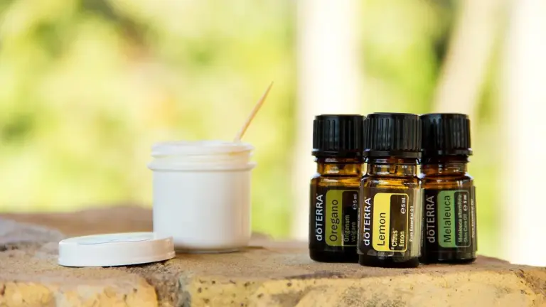 Assorted essential oil bottles and a small jar with a stirring stick on a wooden surface, representing home herbal oil infusion setup.