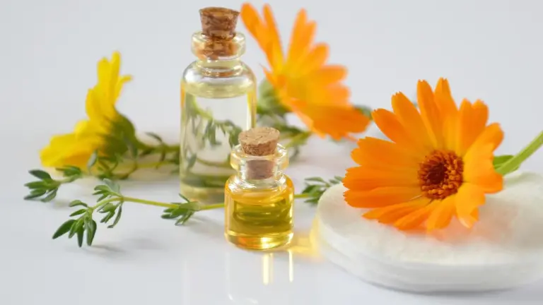 Two small glass bottles of tea tree essential oil with cork stoppers, accompanied by bright orange flowers and a soap bar on a clean white surface.
