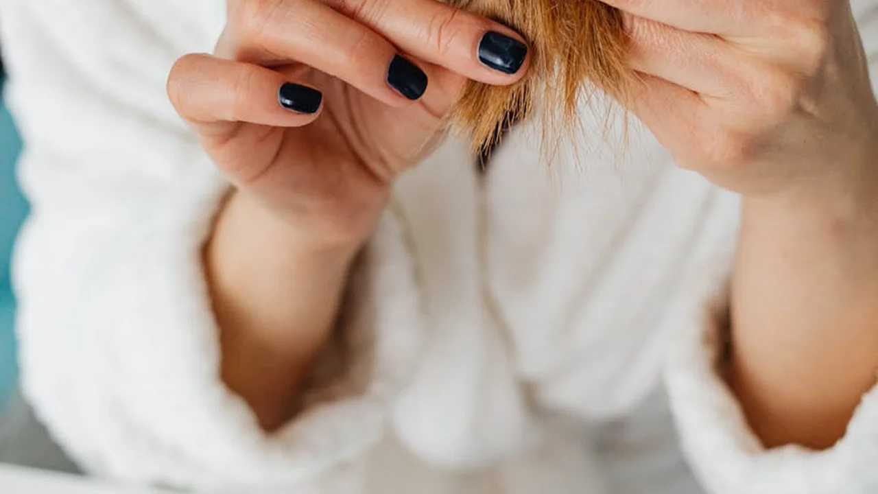 Close-up of a person wearing a white robe with dark nail polish, holding a small brown seed between their fingers