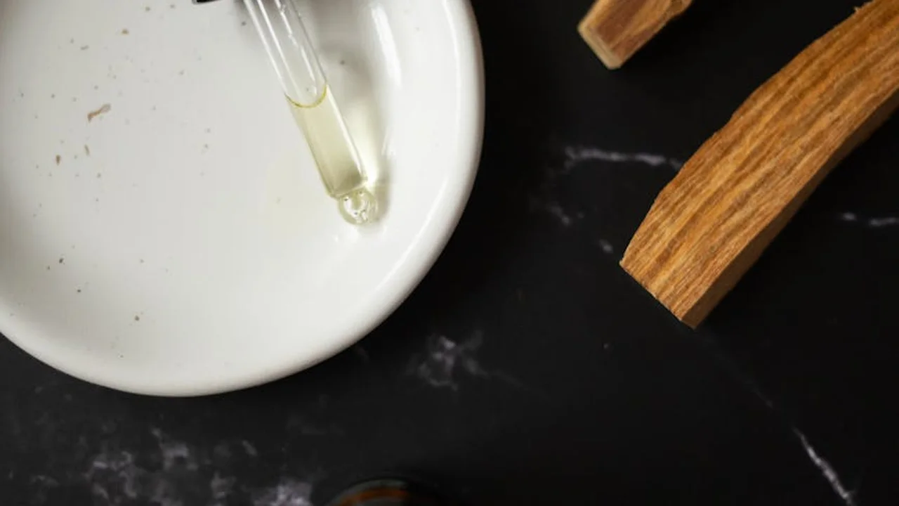 Dropper with clear oil above a white plate on a dark surface, with brown sticks nearby, illustrating skincare oil ingredients to avoid.