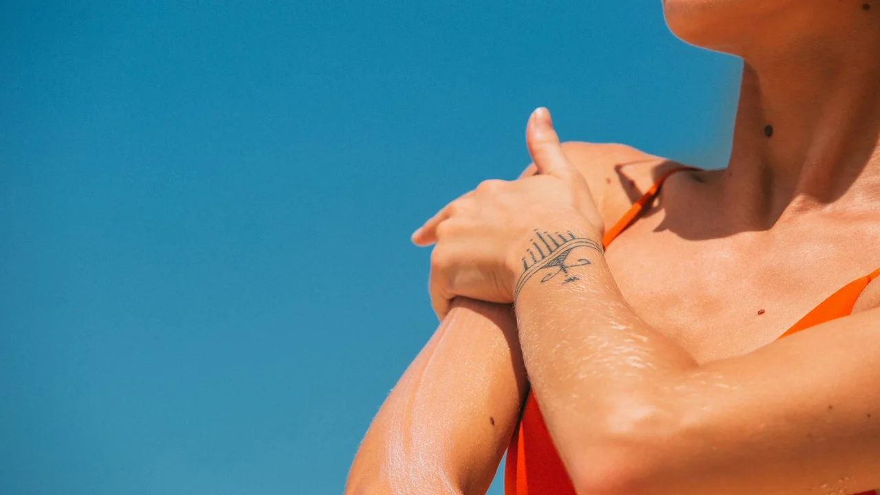 Close-up of a person wearing an orange swimsuit top with arms crossed against a bright blue sky.