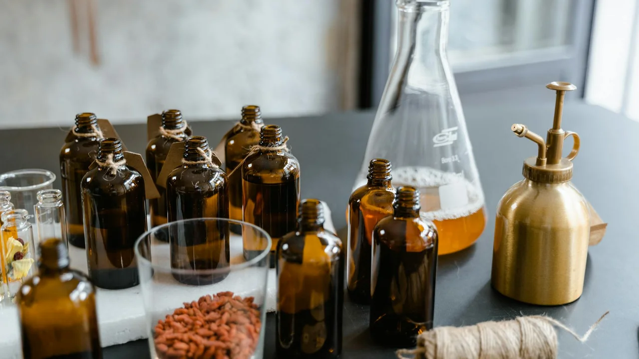 Laboratory bench with amber glass bottles, a glass beaker with orange liquid, and other lab glassware containing oil, illustrating analysis of oils used in skincare and hair products.