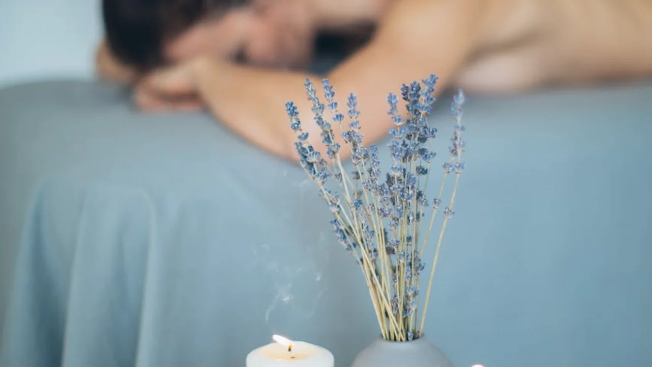 Lavender sprigs in a small vase on a bed with a softly blurred person in the background