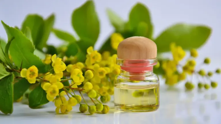 Small glass bottle of essential oil with a pinkish cap on a white surface, with yellow blossoms in the background