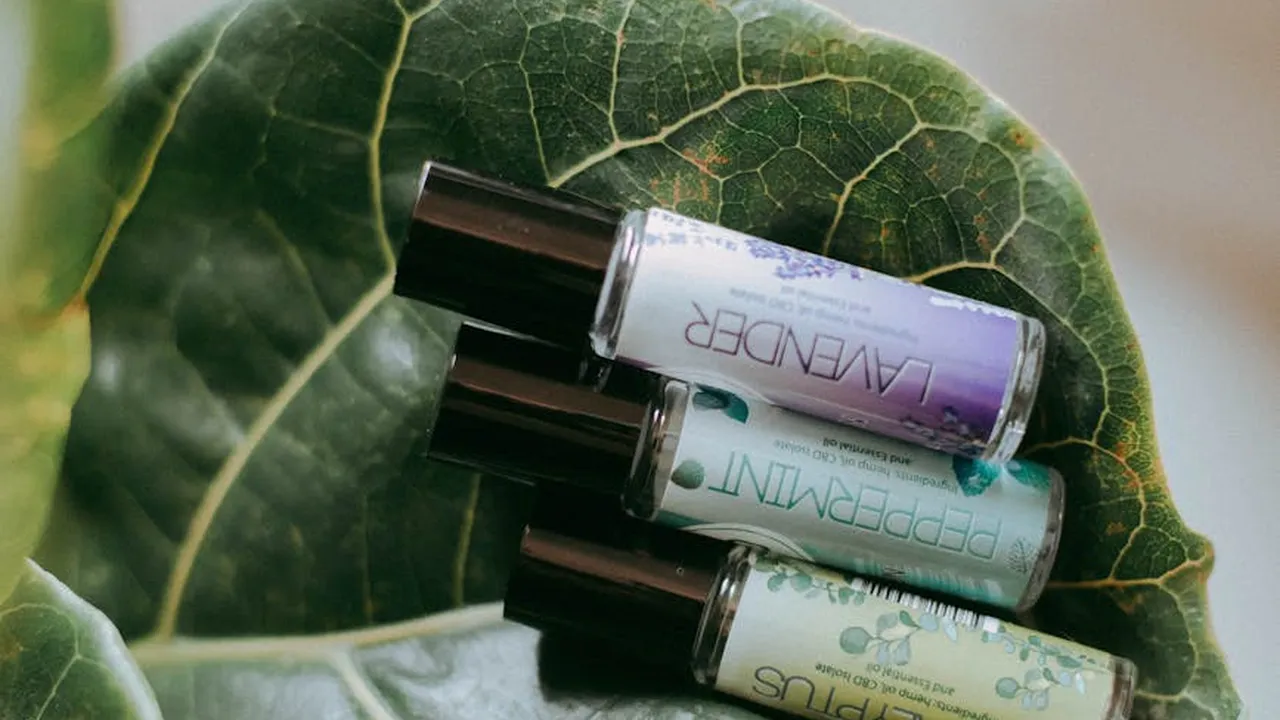 Essential oil roller bottles placed on a large green leaf, with a lavender-labeled bottle clearly visible.