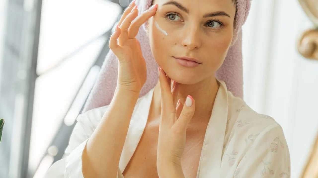 Close-up of a woman applying cream to her face, illustrating skincare decisions related to comedogenic oils.